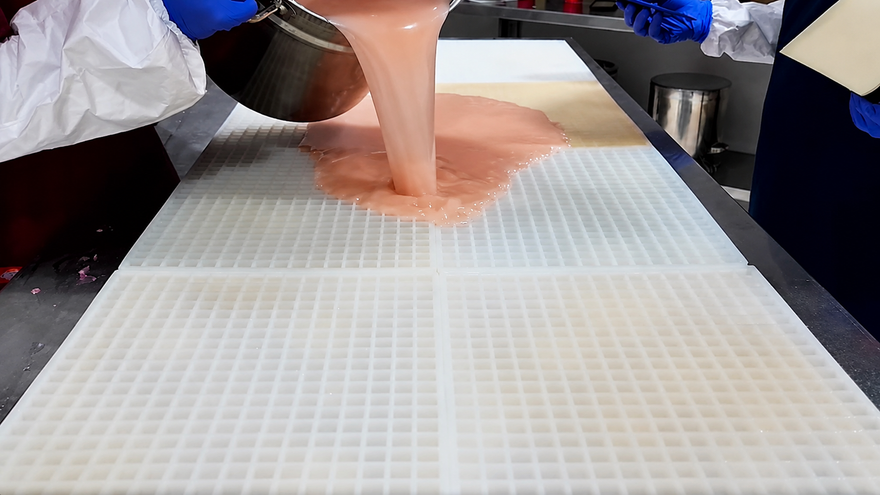 Équipe Gummy Molds versant le mélange de gummies sur un grand moule commercial en silicone avant raclage