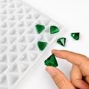 Hand holding an emerald green diamond gummy beside a 2mL diamond gummy mold with 179 cavities on a white background