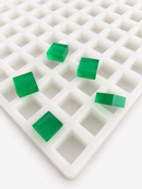 Angled close-up of 4mL Square Gummy Mold - 100 Cavities with translucent emerald green square gummies on a white background
